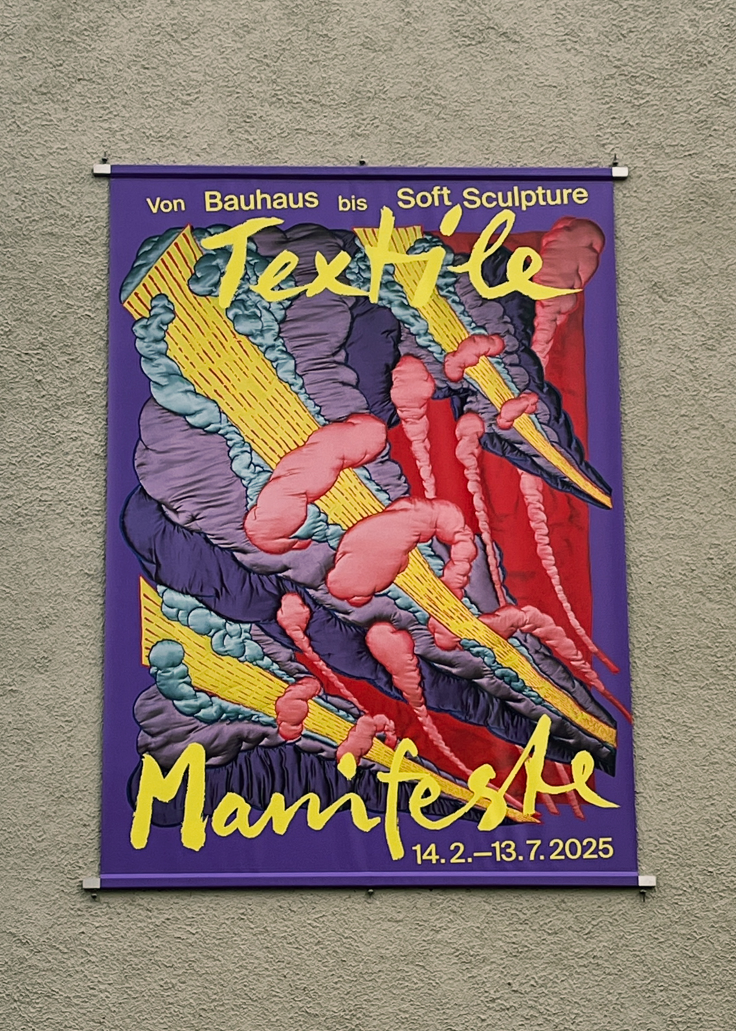 Bedruckter Banner mit grafischem Ausstellungsplakat für die Ausstellung Textile Manifeste, montiert an einer Betonwand
