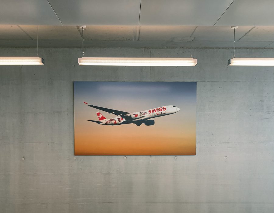 Grossformatiger Plattendruck mit Swiss Flugzeug auf Dibond an einer Betonwand im Innenbereich